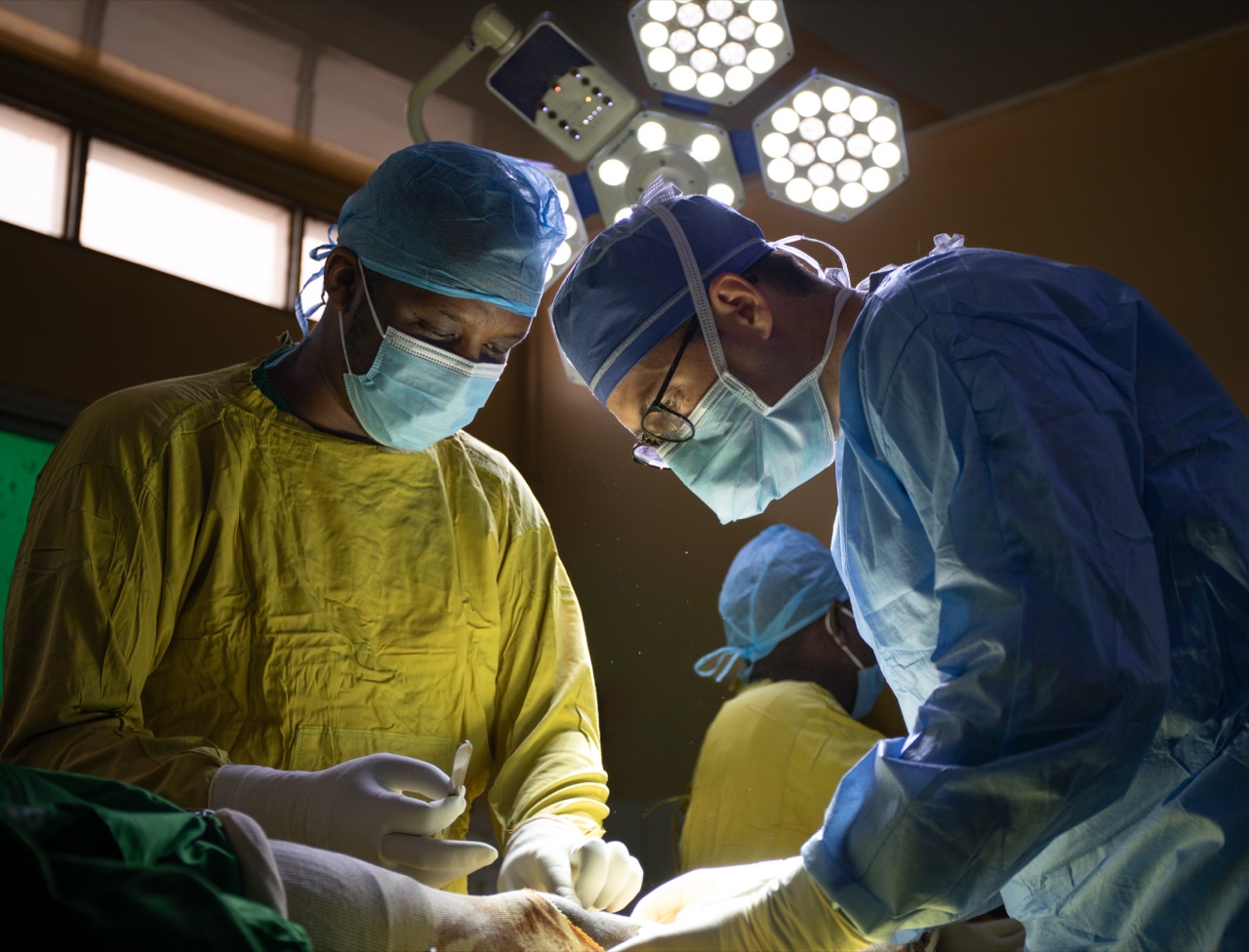 Two orthopedic surgeons working under operating-room lights during a lower-extremity procedure